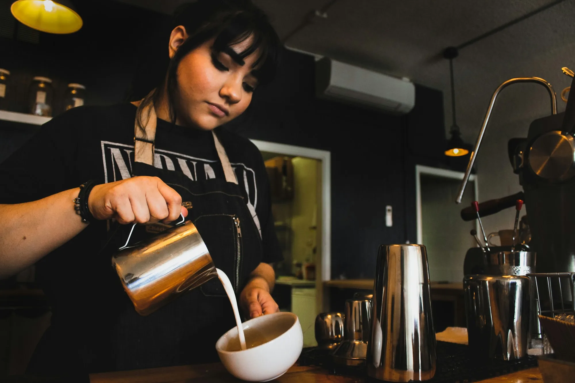 Barista pouring milk into a cup behind a cafe counter