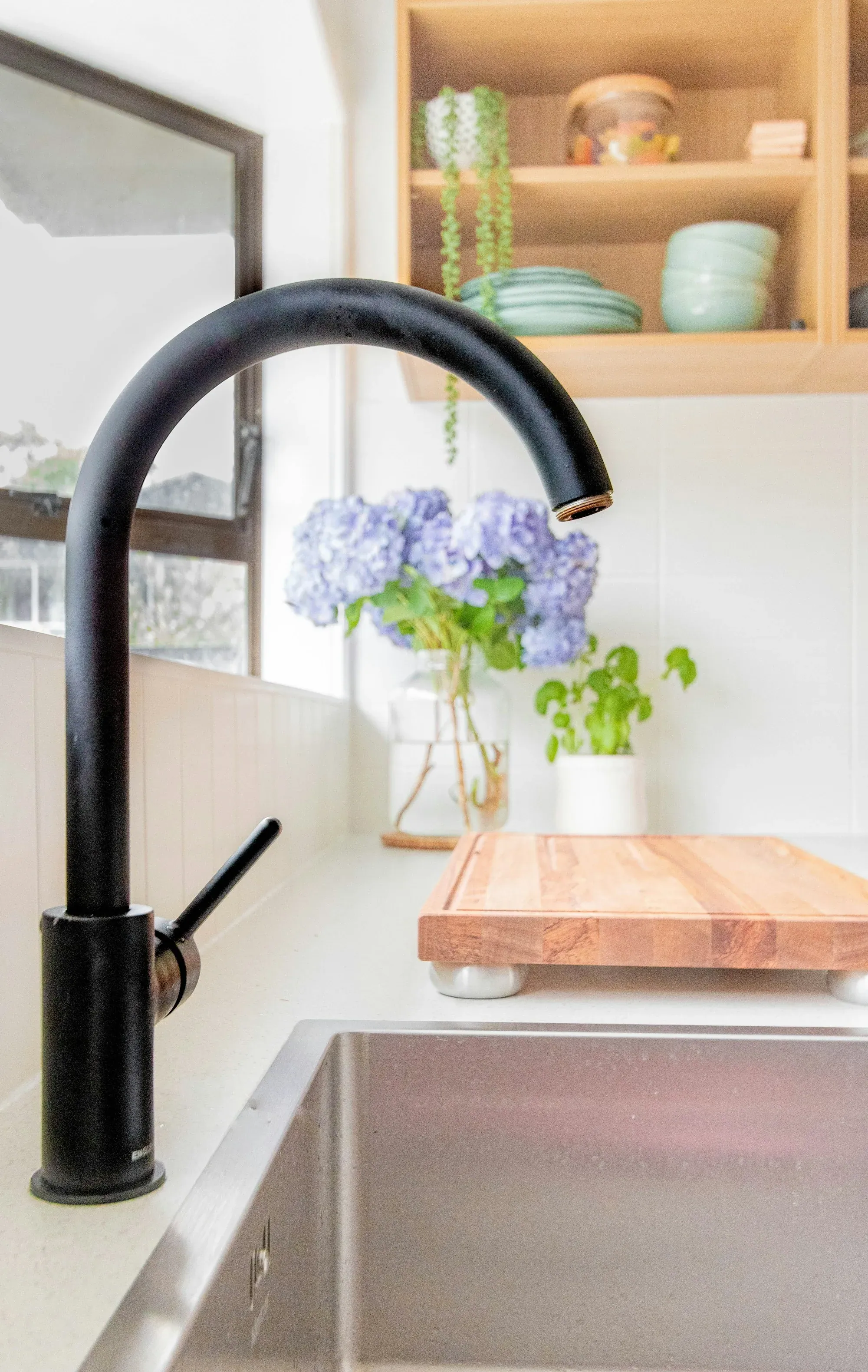 Curved black faucet above a kitchen sink with flowers behind