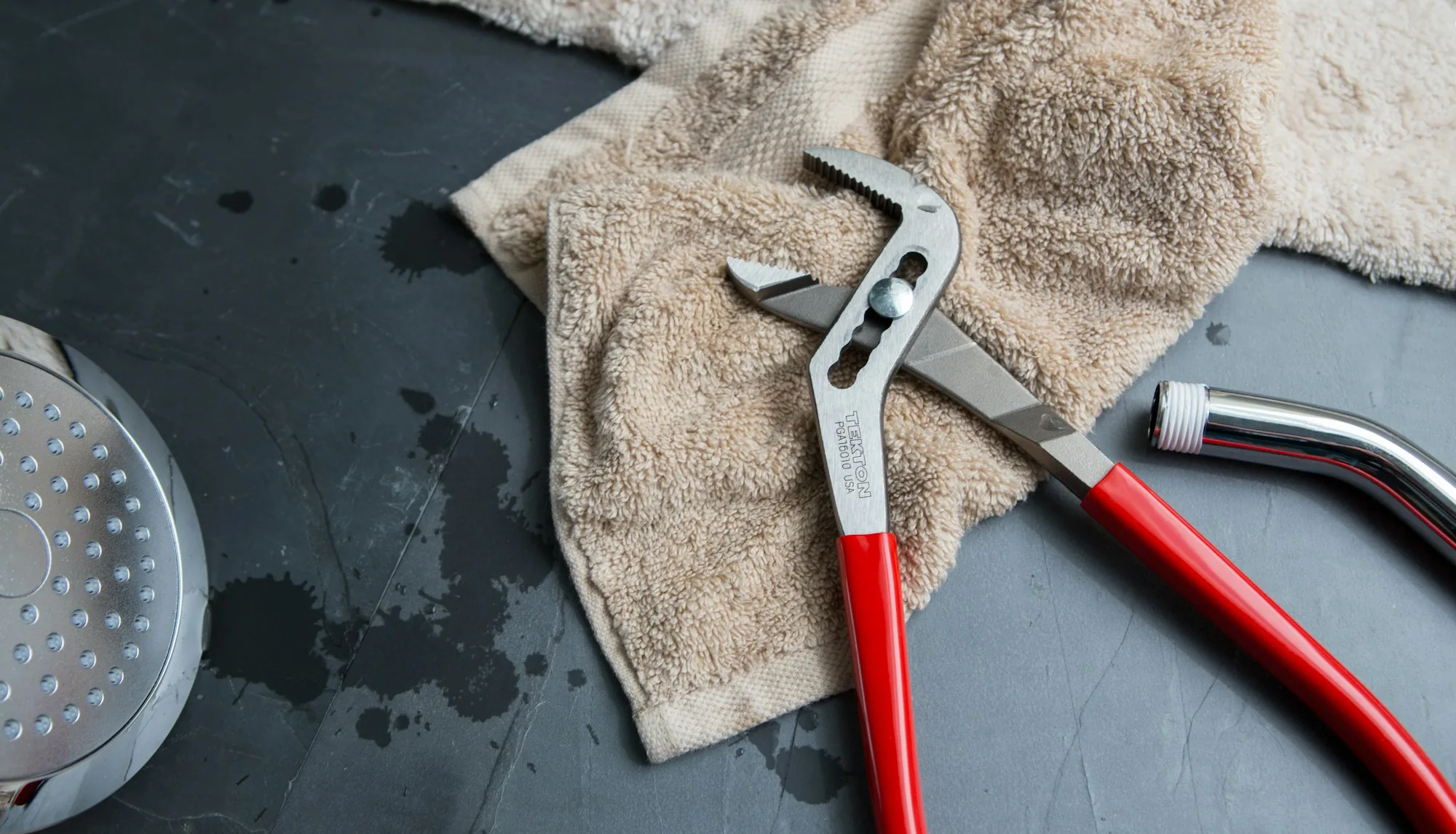 Pliers and a showerhead laid out on a slate work surface