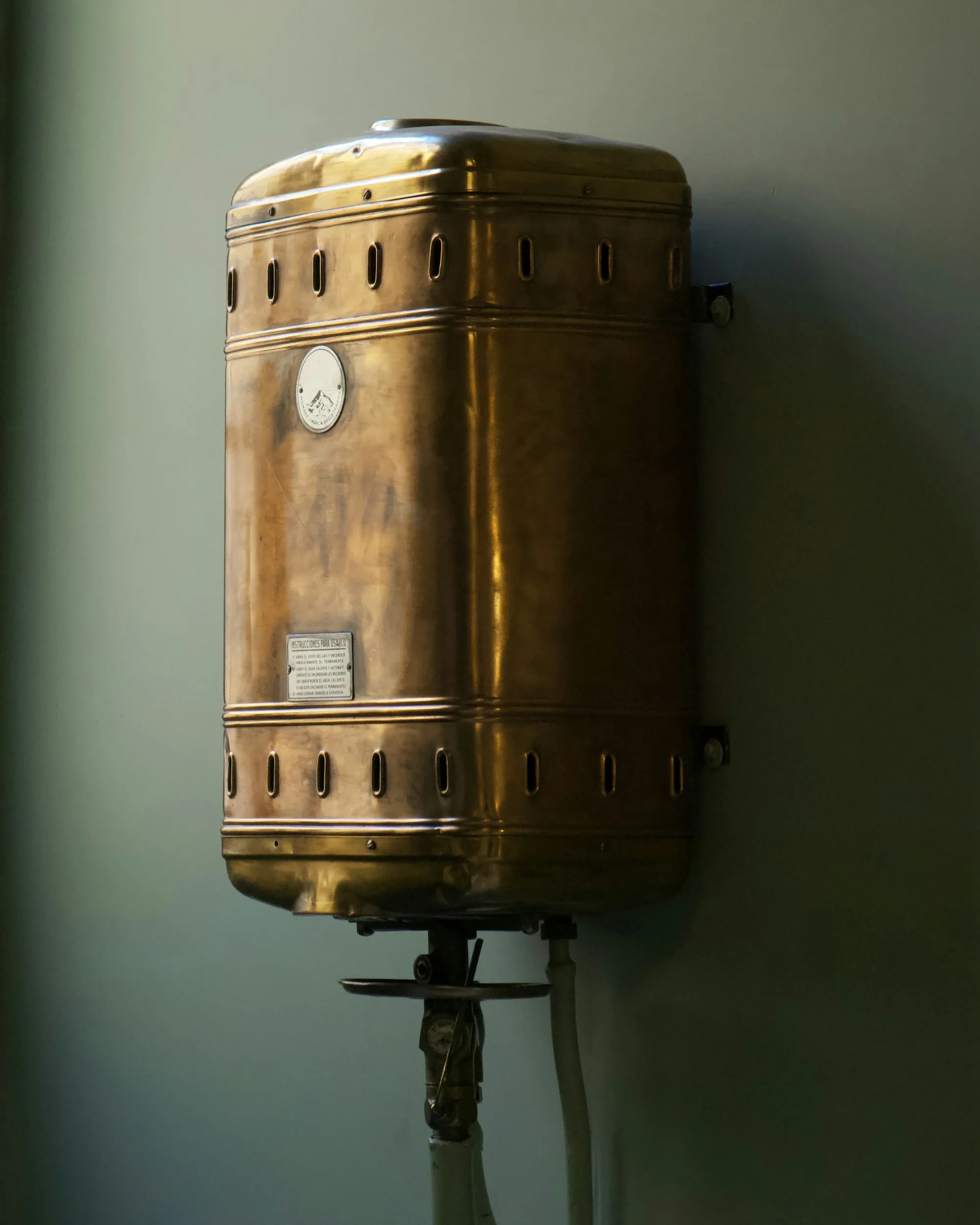 Brass cylinder water heater mounted against a plain wall