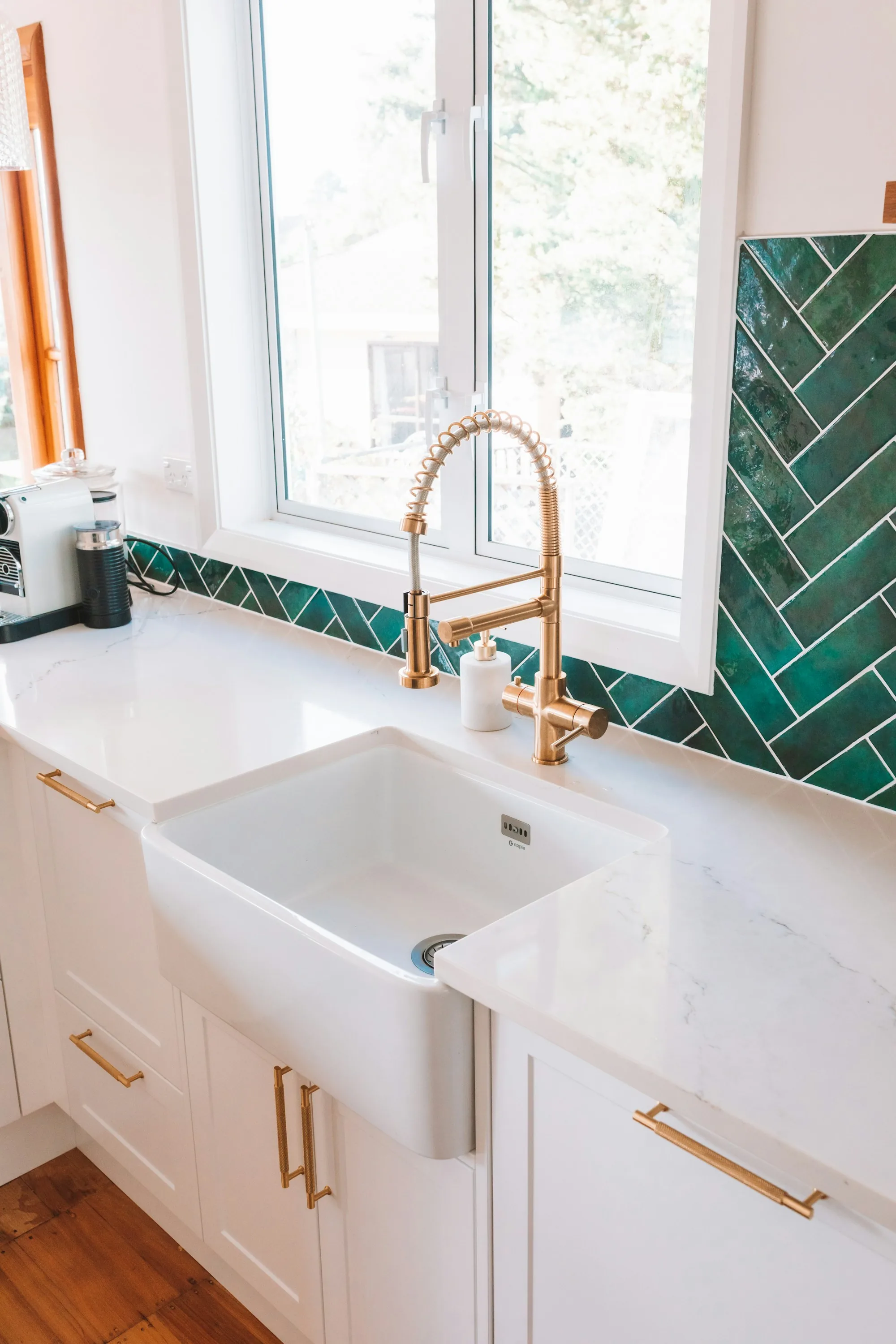 Farmhouse sink and gold faucet against green tile