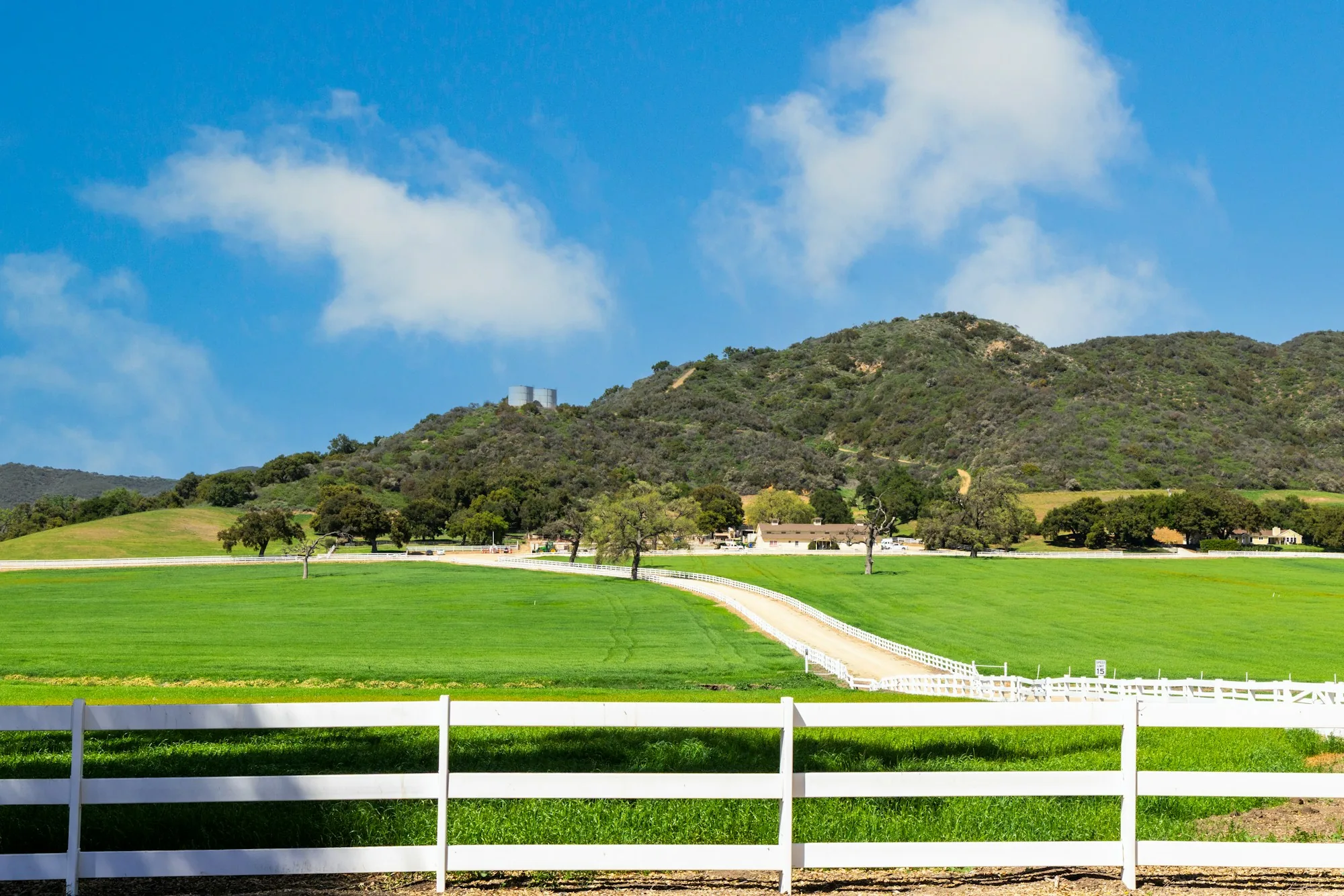 Fenced ranch property with green pasture and hills behind